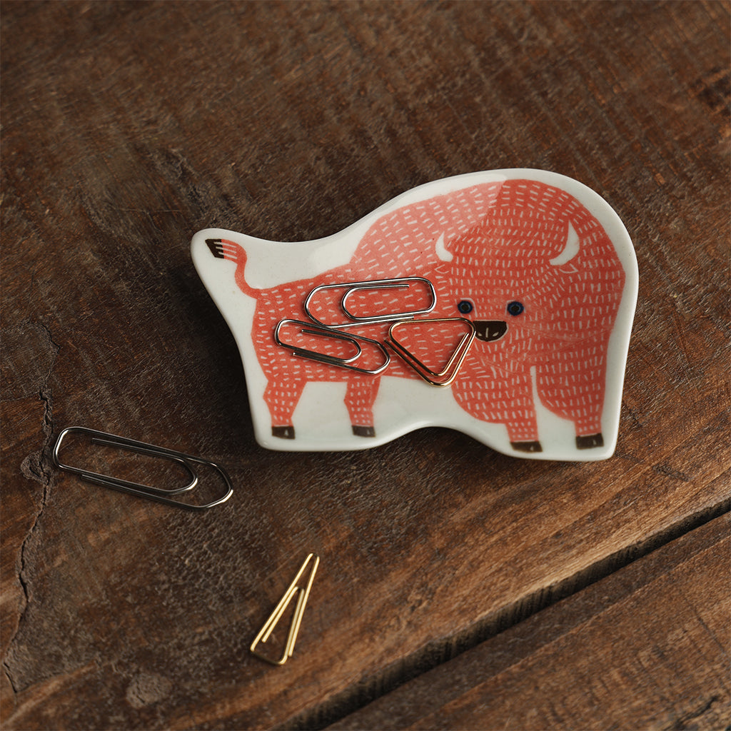 Coral bison-shaped ceramic dish with a textured design holding paperclips. 
