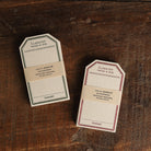 Two packs of tag-shaped cream letterpress stationery cards, one with a green border and one with a red border.