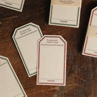 Tag-shaped cream letterpress stationery cards scattered on a wooden desk. 