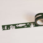 A roll of dark green washi tape with a white cartoon character pattern, partially unrolled on a plain off-white background.
