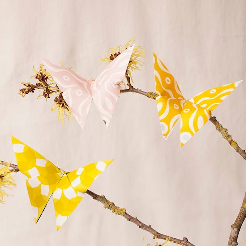 Three paper butterflies on branches against a beige background