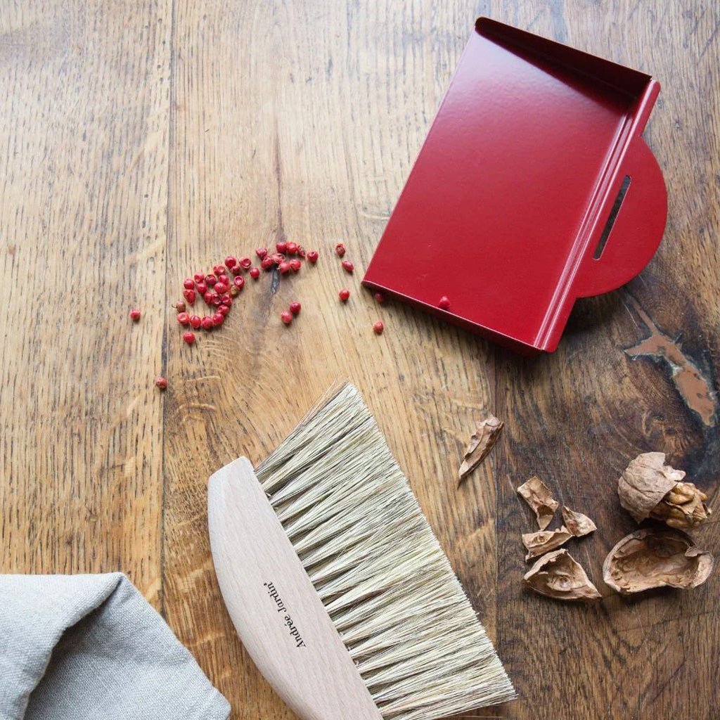 Red dustpan and brush on a wooden surface with scattered items