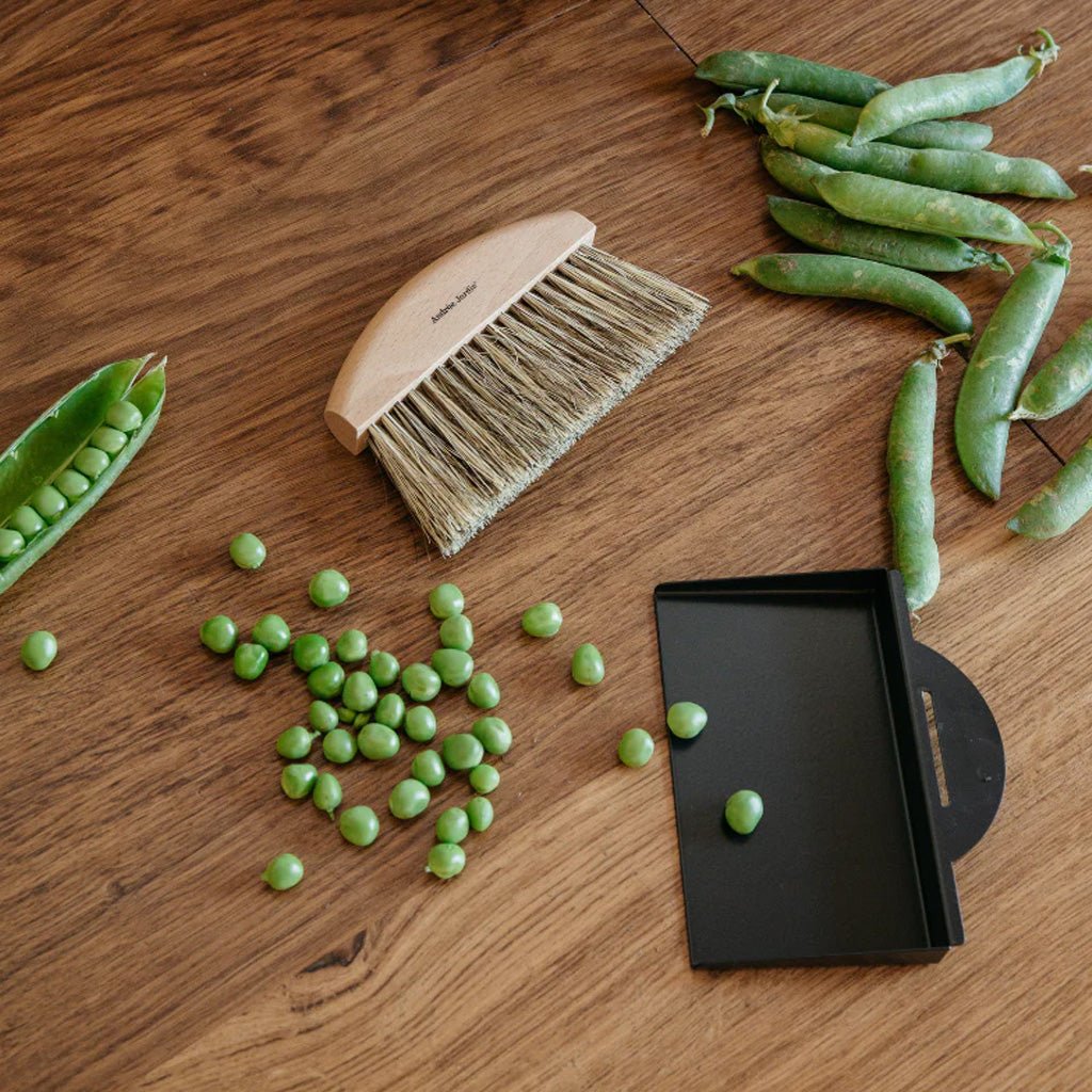 Table brush and tray on a wooden surface with green peas
