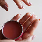 Hand holding open tin of rose salve.