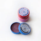 Three metal tins of lip salve, with one propped open.