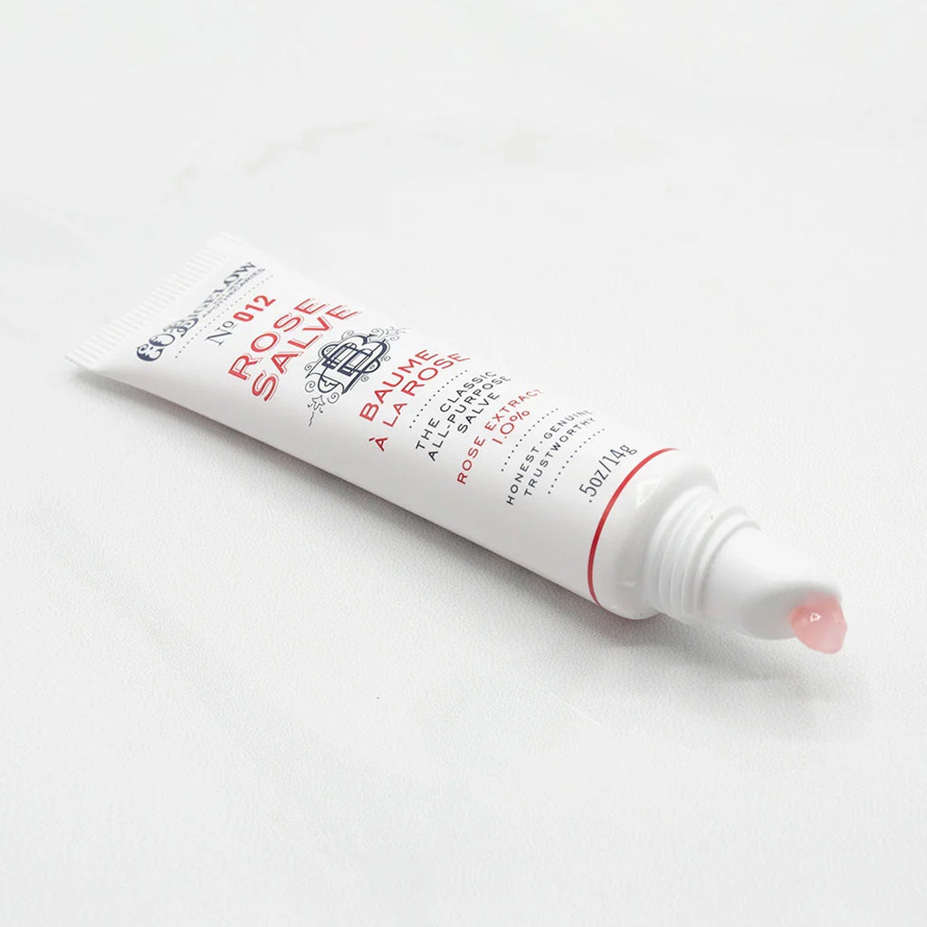 Open tube of rose salve with droplet on tip of applicator.