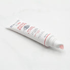 Open tube of rose salve with droplet on tip of applicator.
