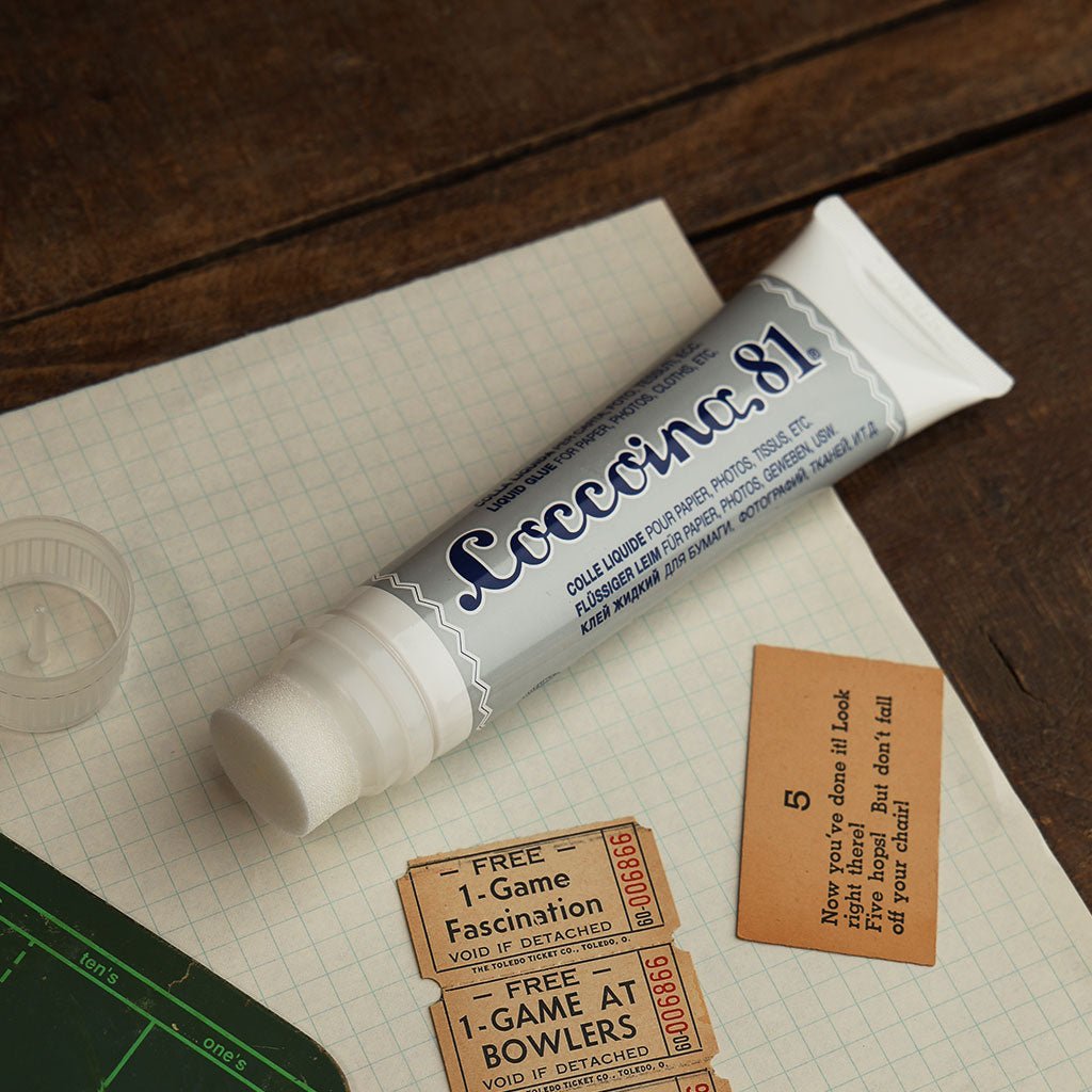 Open tube of Coccoina 81 liquid glue laying on desk with paper