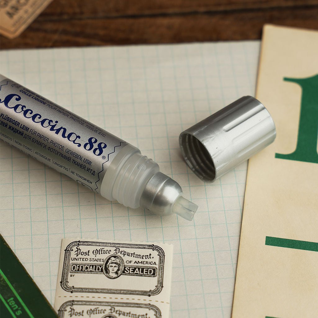 Open tube of Coccoina 88 liquid glue laying on desk with paper