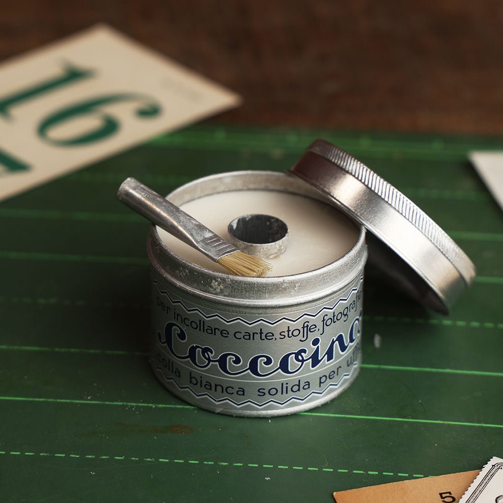Open tin in of Coccoina adhesive paste on a green chalkboard