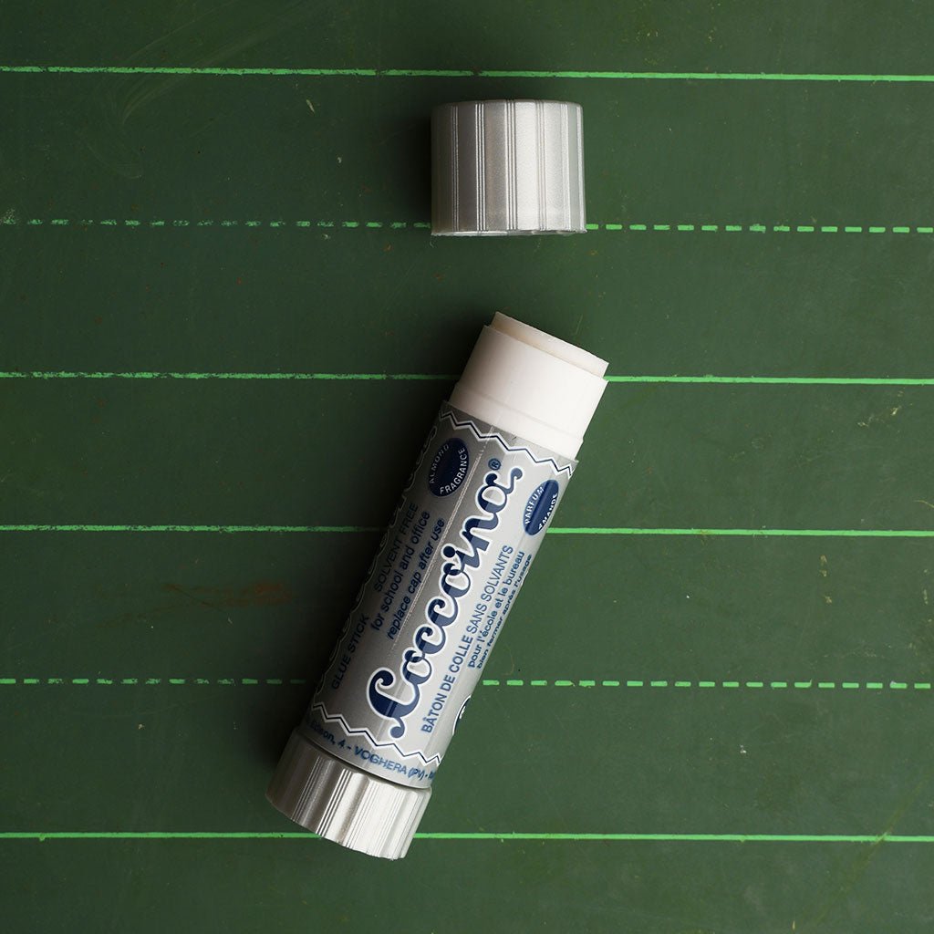 An open coccoina adhesive stick on a green chalkboard 