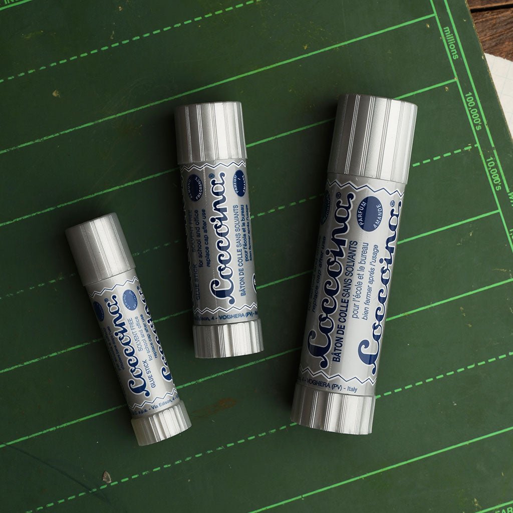 Three coccoina adhesive sticks of different sizes on a green chalkboard 
