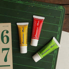 Three colored tubes of Coccoina Mia White Vinyl Glue Adhesive on a green chalkboard