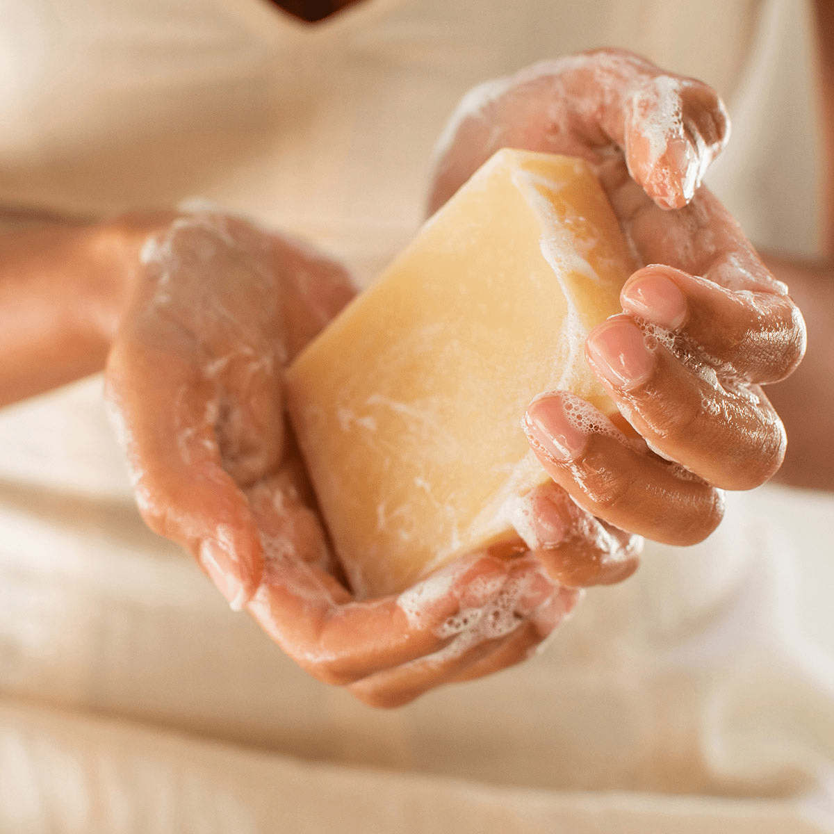 Hand holding a bar of sudsy soap with a soft focus background