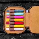 Set of colorful Kaweco pens in a brown leather case on a dark wooden surface