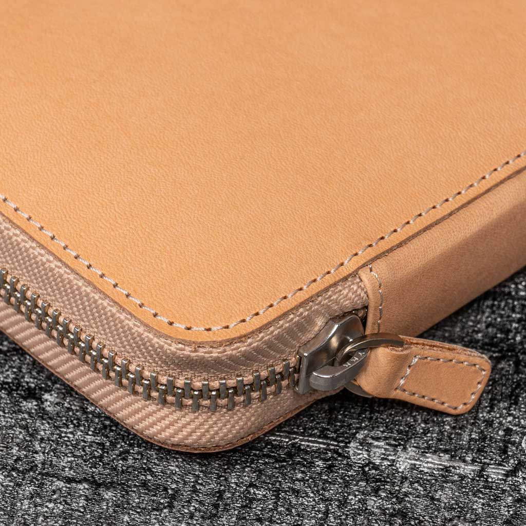 Close-up of a natural undyed leather pen case with a zipper on a textured black surface