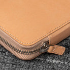 Close-up of a natural undyed leather pen case with a zipper on a textured black surface