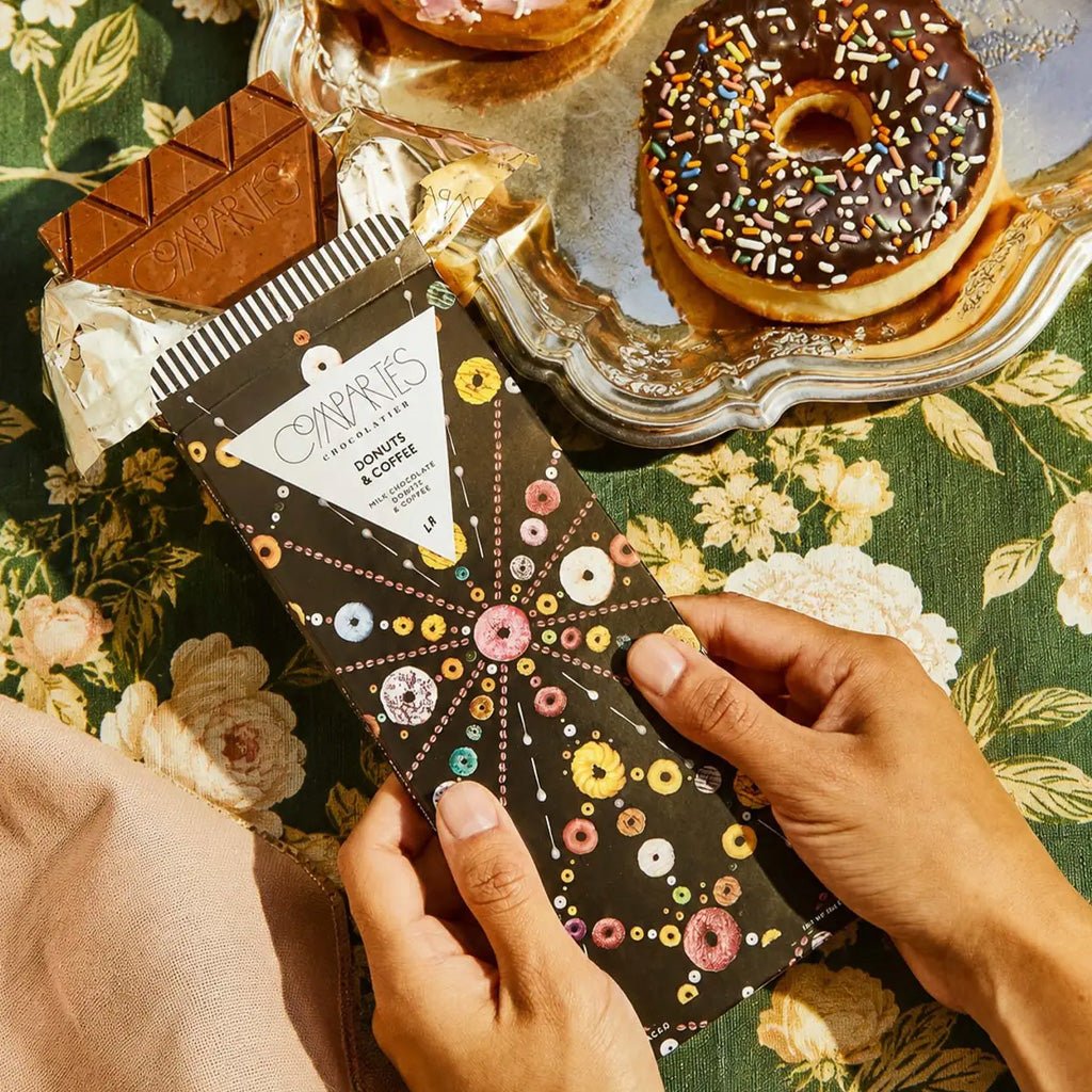 Hands holding chocolate bar next to platter of donuts.