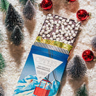 Hot cocoa & marshmallow chocolate bar on holiday-themed background.
