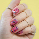 Hand wearing pink nail polish with rainbow confetti cake glitter top coat against yellow background