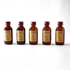 Five small brown bottles with red caps of El Guapo mixers on a white background