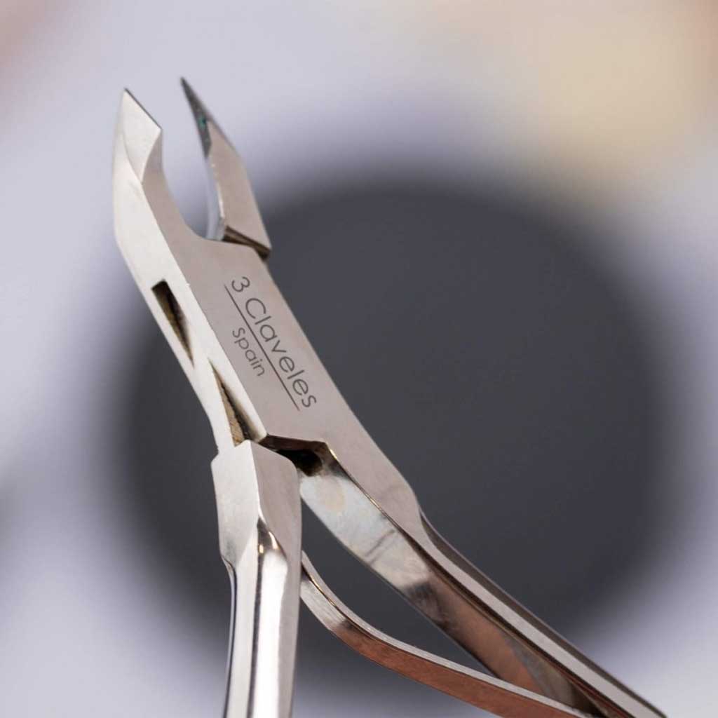 Metal nail clippers with '3 Claveles' branding on a blurred background