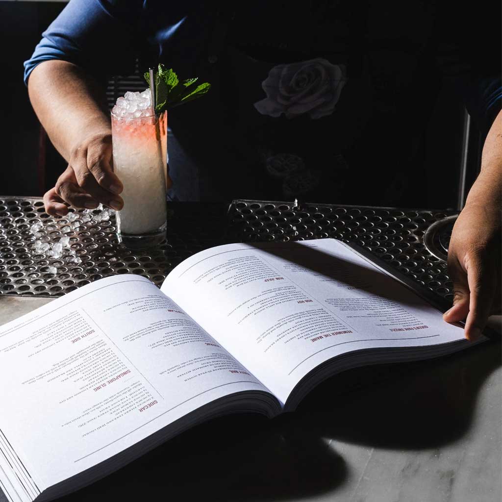 Open book on a table with a drink and laptop in the background