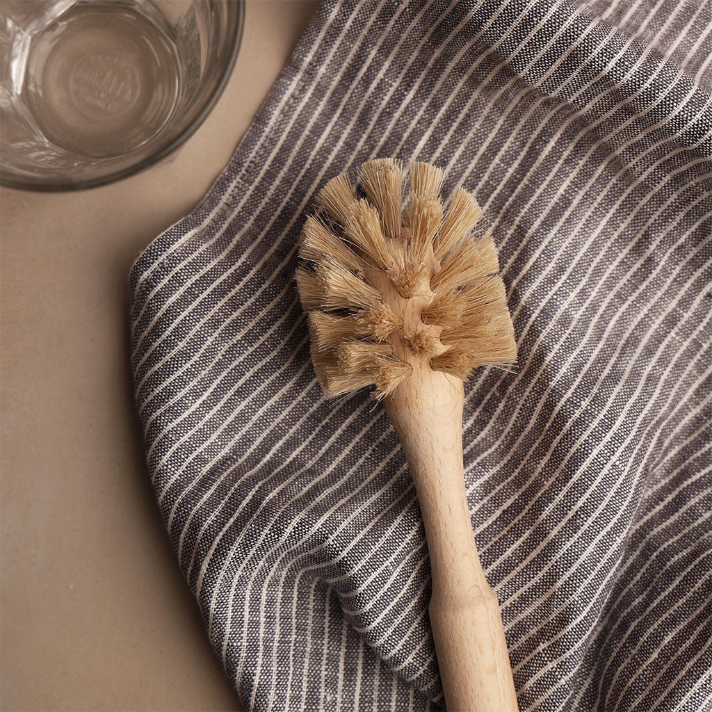 Dish brush on a striped towel with a drinking glass in the background