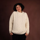 Person wearing a cream cable knit sweater against a brown background