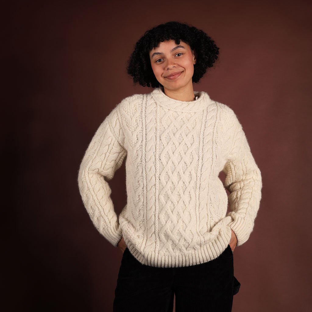Person wearing a cream cable knit sweater against a brown background