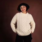 Person wearing a cream cable knit sweater against a brown background