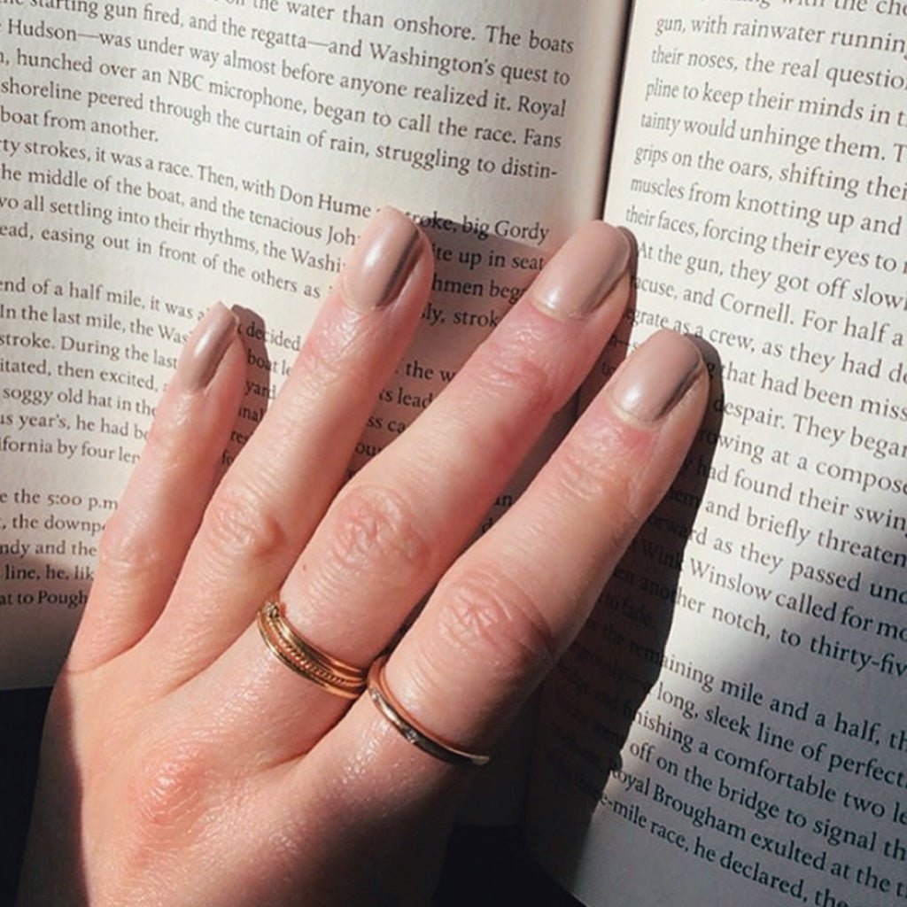 Hand wearing Earl Grey nail polish against open book