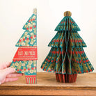 Hand holding folded paper decoration next to open tree decoration.