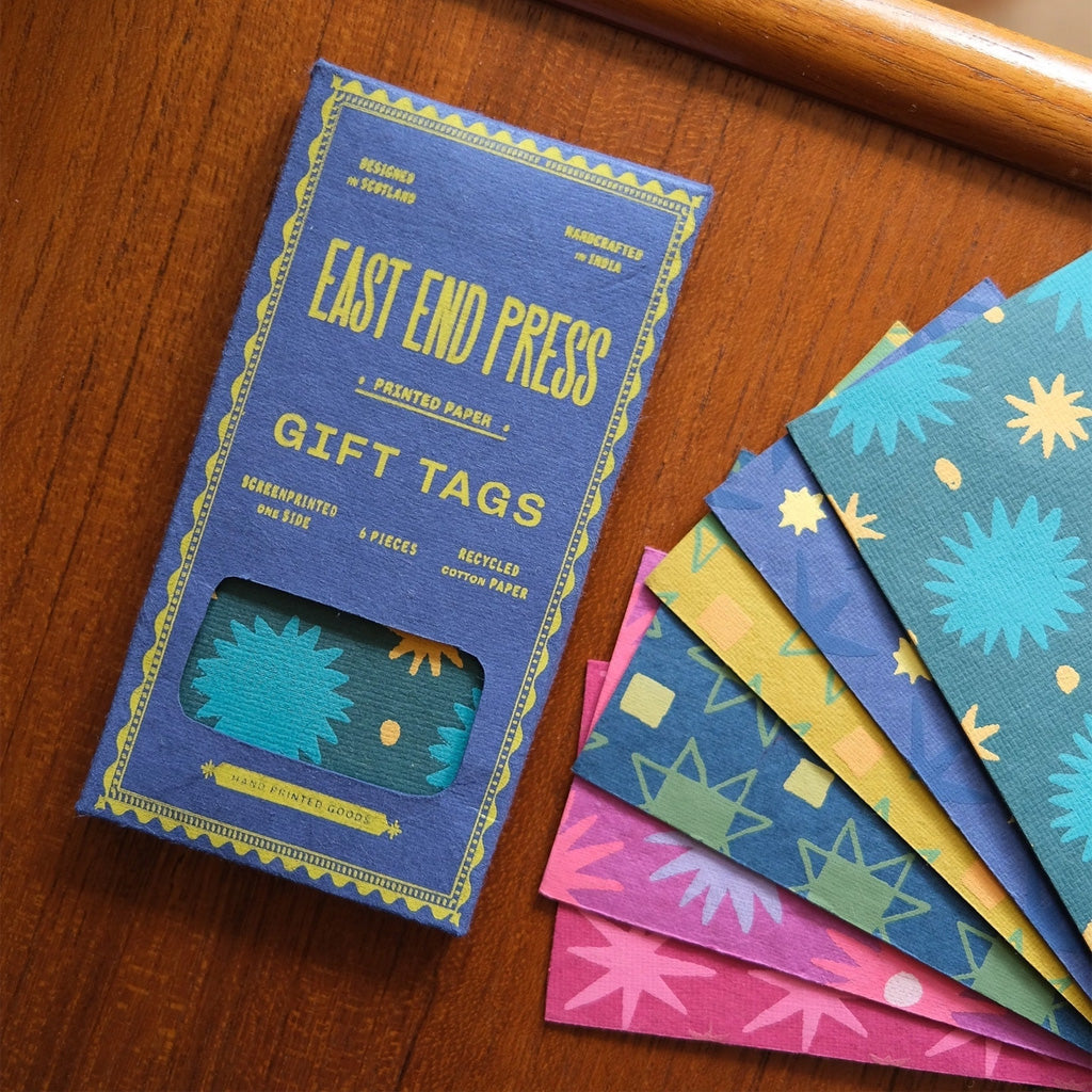 Box of gift tags next to tags laying on wooden table.