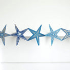 Blue star concertina garland hanging on white wall.