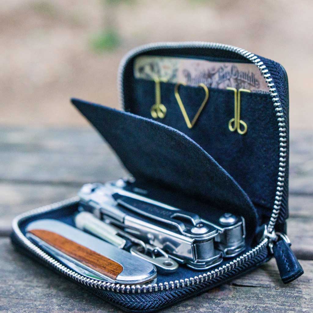 Black zipper wallet with tools on a wooden surface