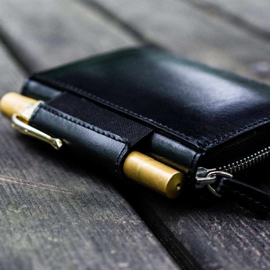 Black leather wallet with gold pen on a wooden surface