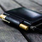 Black leather wallet with gold pen on a wooden surface