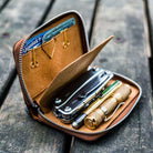Open brown leather wallet with tools on a wooden surface