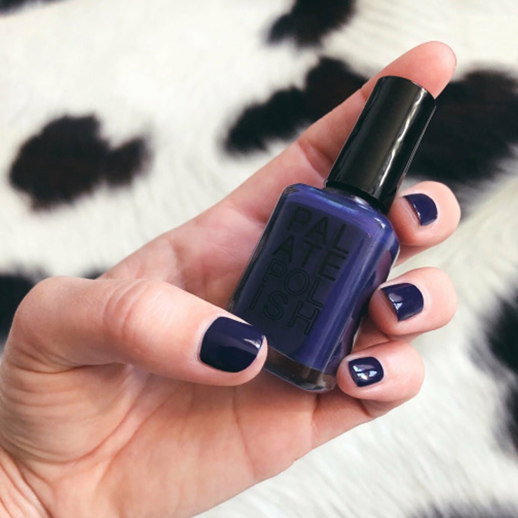 Hand wearing purple nail polish holding Palate Polish bottle against cow-printed rug