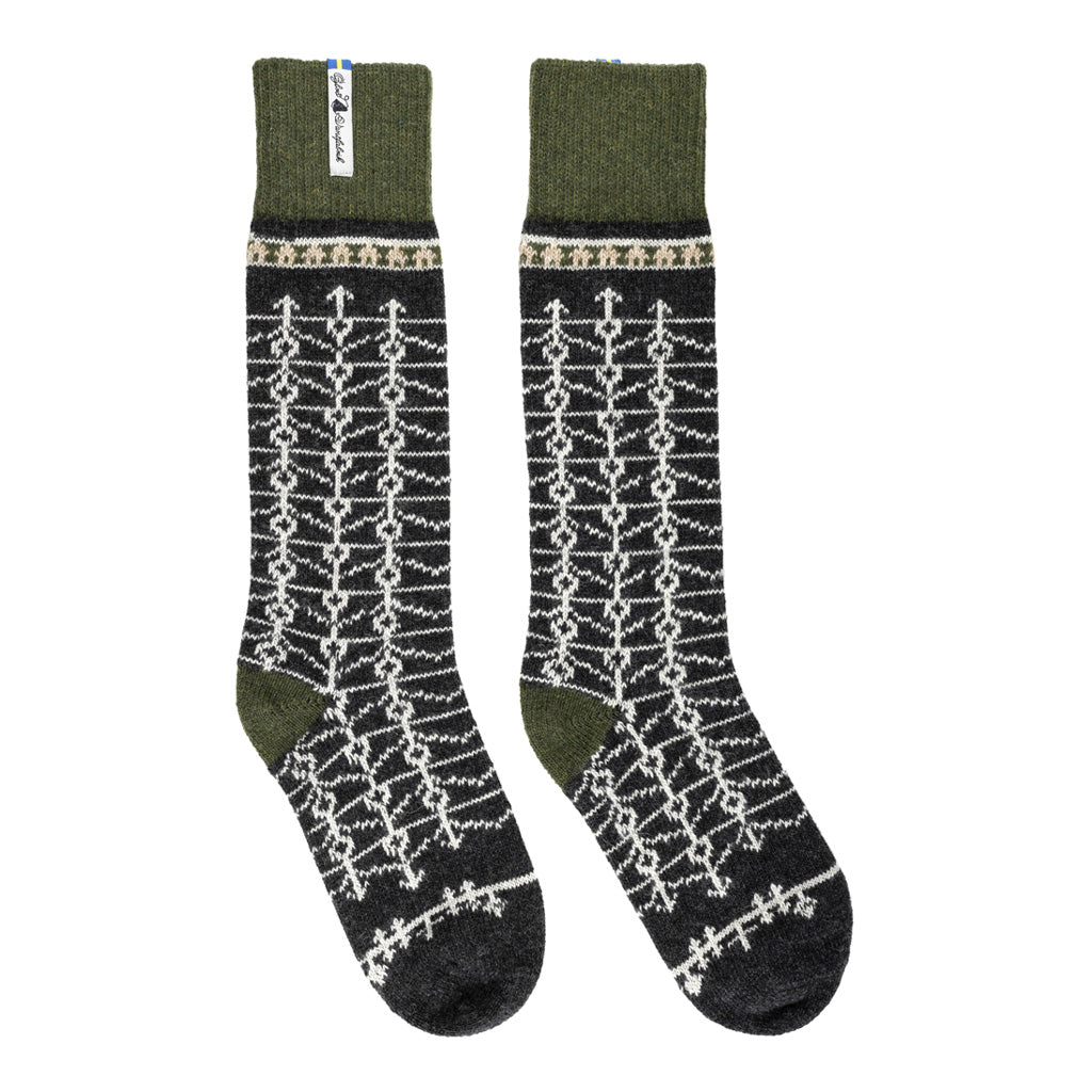 A pair of tall wool socks with a dark charcoal gray base, featuring a white geometric knit pattern and olive green cuffs and heels, displayed against a plain white background.