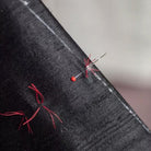 Black fabric with red thread, tailor's chalk, and a needle on a neutral background