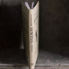 Book titled 'Elementary Sewing Skills' on a wooden surface with a dark background