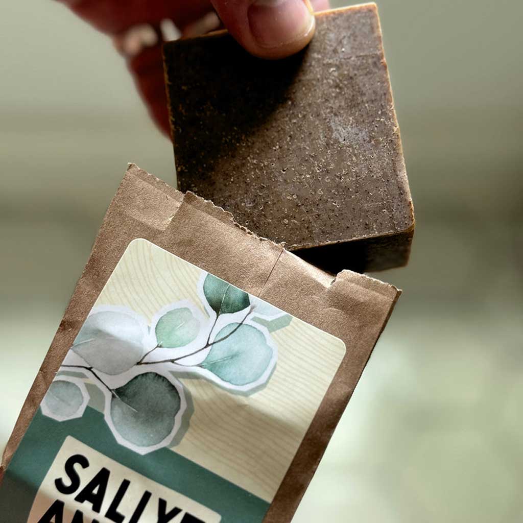 Bar of SallyeAnder eucalyptus soap being pulled out of packaging against green background