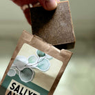Bar of SallyeAnder eucalyptus soap being pulled out of packaging against green background