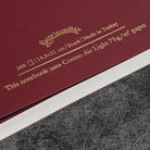 Maroon notebook with gold text on a gray surface
