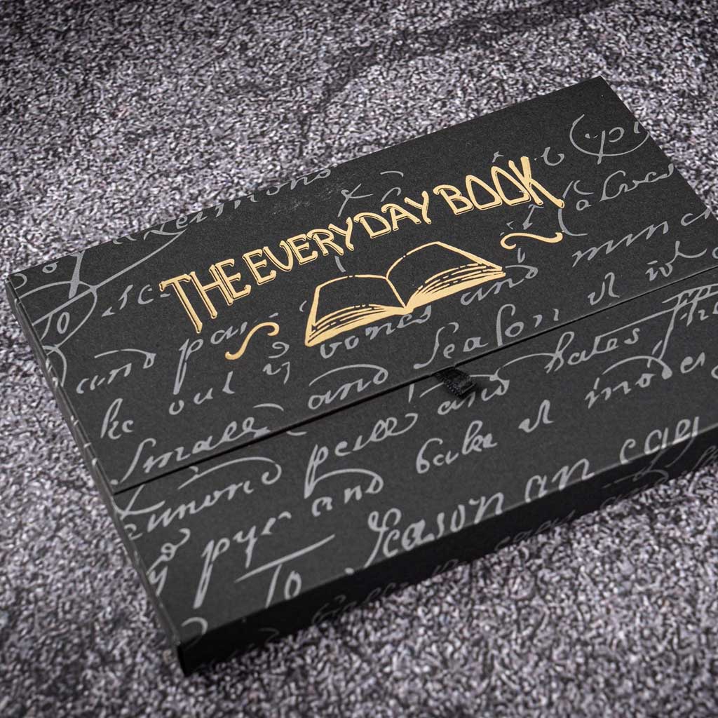 Black notebook box with gold branding and gray design on dark textured surface