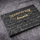 Black notebook box with gold branding and gray design on dark textured surface