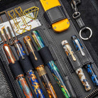 Collection of pens and accessories in a black leather case on a textured surface
