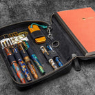 Collection of pens and a notebook in a black leather case on a textured surface